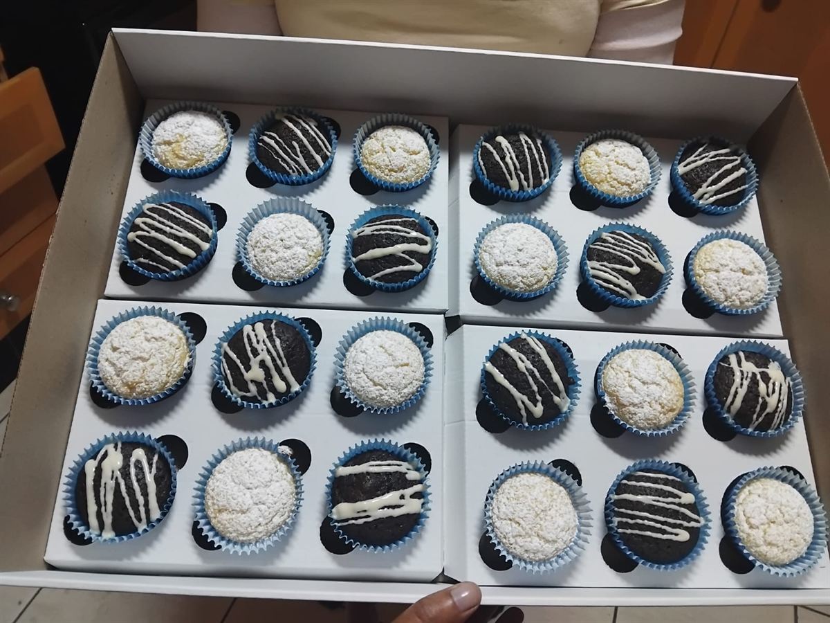 Tray of chocolate cupcakes with white drizzle and vanilla cupcakes dusted with icing sugar